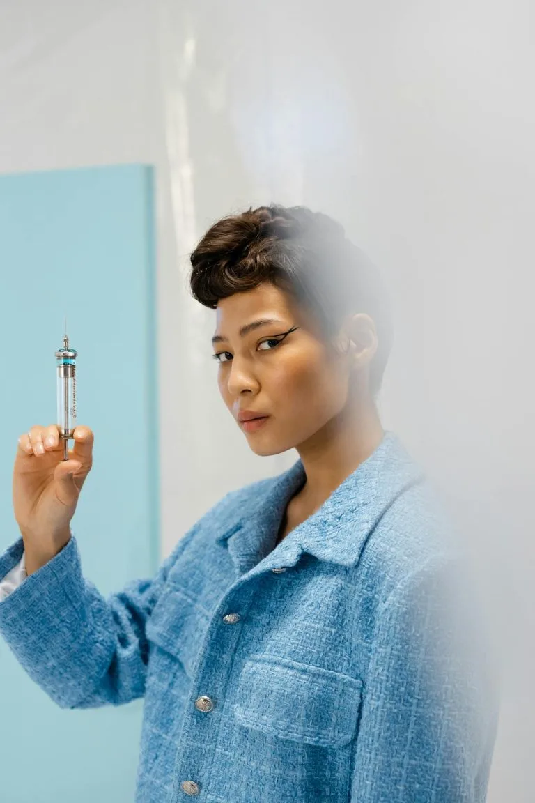 Stylish woman in blue holding syringe, featuring a modern studio backdrop.