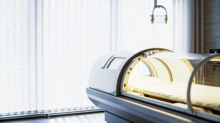 A hyperbaric oxygen therapy chamber in the spotlight, next to a window in a medical clinic.